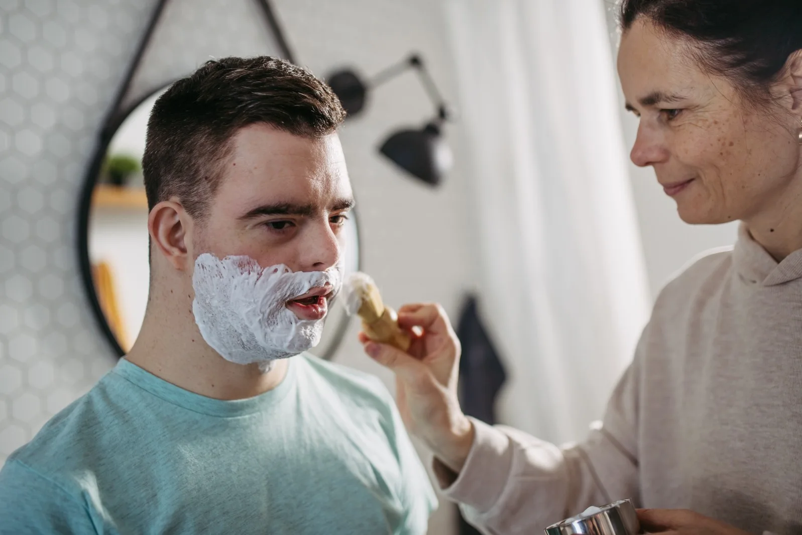 Disabled man with down syndrome having assistance shaving from support worker